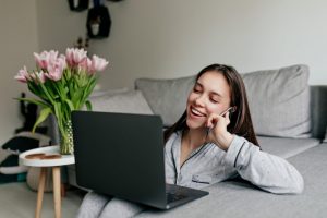 happy-smiling-woman-in-pajamas-talking-on-the-phone-and-working-with-laptop-at-modern-stylish-apartment-on-quarantine-1024x683